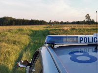 Widoczny dach policyjnego radiowozu na tle pół, w oddali widać skodę