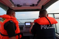 Dwóch policjantów w pomarańczowych kamizelkach płyną sterami policyjnej łodzi