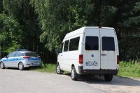 Biały bus oraz oznakowany radiowóz stojące na poboczu drogi
