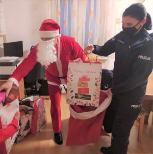 Św. Mikołaj i policjantka przekładają torby z prezentami