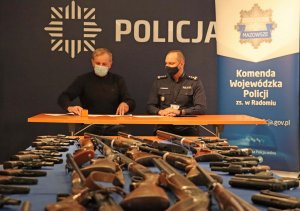 Dwaj mężczyźni siedzący za stołem, przed nimi stół z bronią