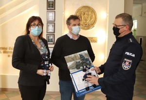 Umundurowany policjant oraz dwie osoby cywilne w maseczkach