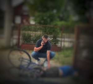 Mężczyzna pochylony nad lezącym rowerzystą powiadamia przez telefon służby ratunkowe