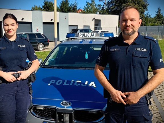 Dwoje policjantów stojących przy radiowozie.
