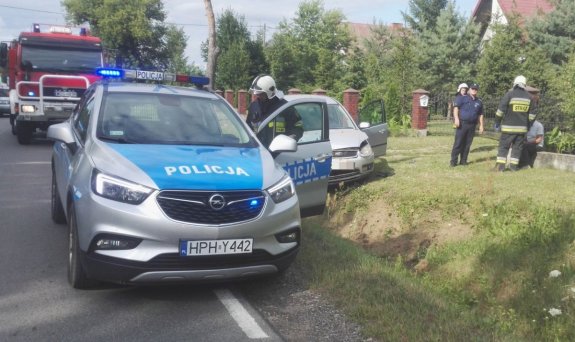 Na pierwszym planie radiowóz, w tle rozbite auto oraz osoba poszkodowana
