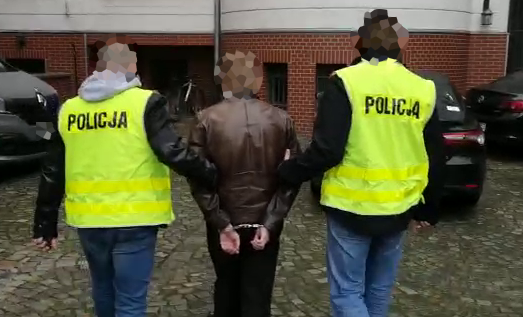Dwaj policjanci w kamizelkach odblaskowych prowadzą zatrzymanego