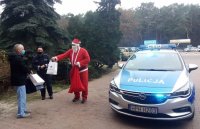 Mikołaj wraz z policjantką przekazują paczki dla dzieci ordynatorowi obok policyjnego radiowozu przed Szpitalem Powiatowym w Kozienicach
