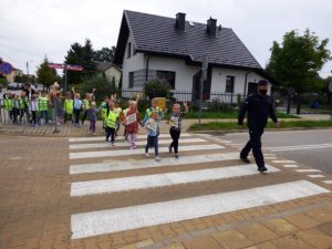 policjant wraz z dziećmi przechodzą przez przejście dla pieszych