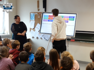 nauczycielka, uczniowie i uczeń stojący przy tablicy interaktywnej na której znajdują się kolorowe  rysunki