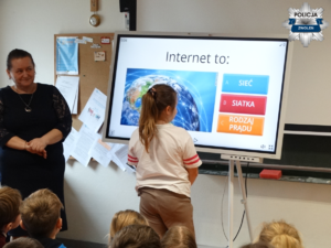 nauczycielka, uczniowie i uczennica, która stoi przy tablicy interaktywnej na której pisze Internet to A sieć B siatka  C rodzaj prądu