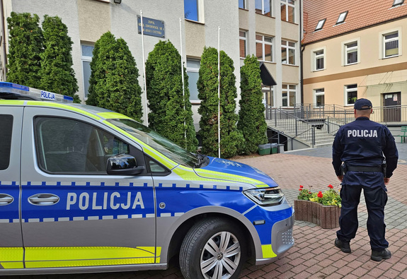 umundurowany policjant obok radiowóz a w tle budynek szkoły
