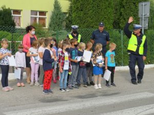 policjant stojący z podniesioną rękom przy grupce dzieci przed przejściem dla pieszych