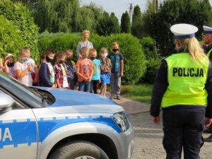 stojący policjanci przed grupą dzieci tłumacząc zasady bezpieczeństwa i noszenia odblasków