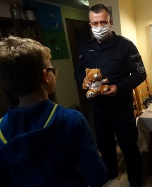 policjant stojący z misiem dający dziecku maskotkę
