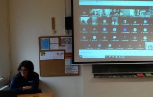 policjantka siedząca przed komputerem i w tle ekran z połączonymi uczniami