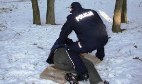 umundurowany policjant nachyla się nad osoba bezdomną leżąca na śniegu