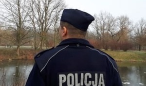 Umundurowany policjant stoi tyłem, w tle rzeka