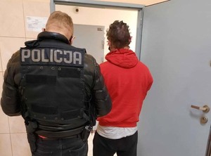 Policjant umundurowany stoi tyłem, obok stoi osoba podejrzana o popełnienie przestępstwa