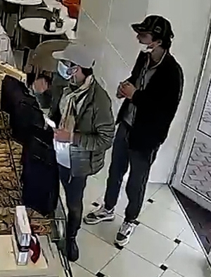 Wizerunek dwóch mężczyzn podejrzewanych o kradzież pieniędzy, stoją w lokalu w czapkach z daszkiem i maseczkach ochronnych
