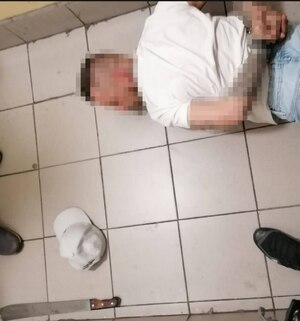 Mężczyzna z założonymi na ręce z tyłu kajdankami leży na ziemi, w tle maczeta.