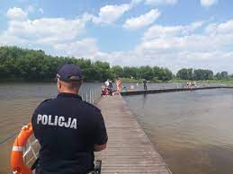 Umundurowany policjant obserwuje rzekę w rejonie plaży miejskiej w Ostrołęce