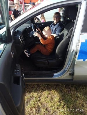 Dziecko siedzi na festynie rodzinnym w radiowozie, obok policjantka