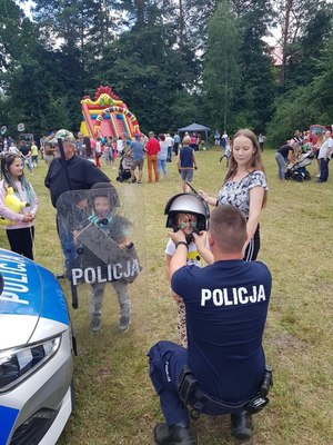 policjant w ramach spotkań podczas festynu pomaga założyć dziecku kask policyjny
