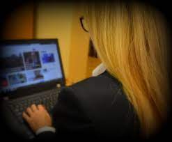 kobieta siedzi tyłem, przed nią stoi laptop