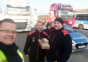 Policjant i członkowie grupy kierowcy dzieciom, w tle dwa ciągniki siodłowe