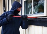 Na zdjęciu zamaskowany mężczyzna próbujący otworzyć okno za pomocą łomu