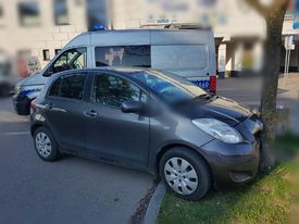 Rozbite auto, które uderzyło w drzewo, w tle policyjny radiowóz