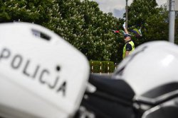 Policjant stoi obok policyjnego motocykla i  zatrzymuje pojazd do kontroli