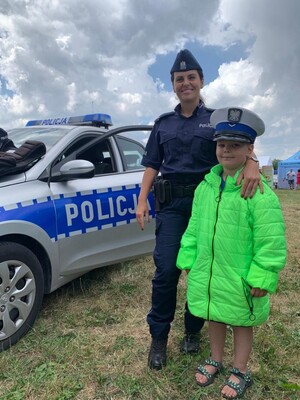 Policjantka umundurowana, obok niej stoi dziewczynka w policyjnej czapce - piknik profilaktyczny