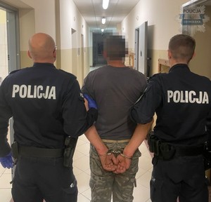 zatrzymany w kajdankach stoi tyłem, obok umundurowani policjanci