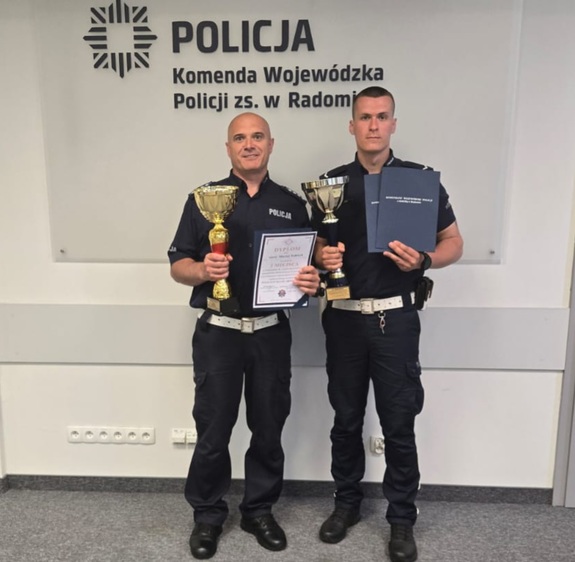 Policjanci trzymają puchary w ręku. Po prawej sierż. Maciej Sobiech, po lewej Zastępca Naczelnika Wydziału Ruchu Drogowego KMP Ostrołęka.