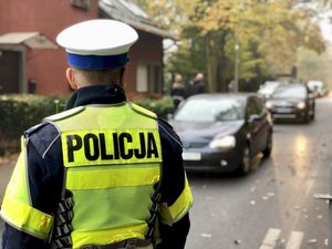 Policjant umundurowany stoi tyłem, w tle auta