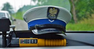 Zdjęcie przedstawiajace policyjną czapkę, która leży na desce rozdzielczej radiowozu, pod nią policyjny alcoblow