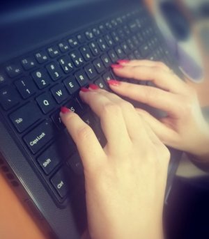 Zdjęcie przedstawia dłonie kobiety piszące na klawiaturze laptopa