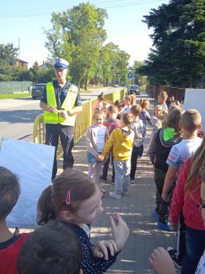 policjant ubrany w kamizelkę odblaskową przy przejściu dla pieszych rozmawia z dziećmi