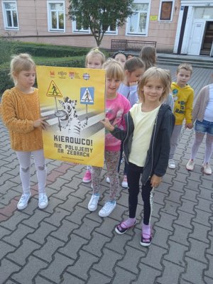 kilka dziewczynek na zdjęciu trzyma w ręku plakat koloru żółtego z napisem Kierowco ! Nie polujemy na zebrach !