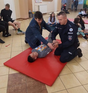 policjant na macie uczy chłopca udzielania pierwszej pomocy