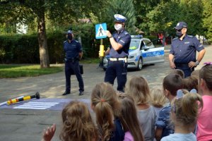 policjant z Wydziału Ruchu Drogowego płockiej komendy prezentuje dzieciom znak informujący o przejściu dla pieszych