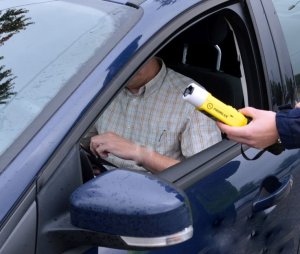 zdjęcie przedstawia policjanta, który wykonuje badanie stanu trzeźwości policyjnym alkomatem kierującego samochodem osobowym