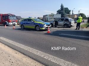 Miejsce zdarzenia drogowego w miejscowości Modrzejowice. Na zdjęciu znajduje się radiowóz policyjny, straż pożarna, uszkodzony pojazd oraz policjant w kamizelce odblaskowej koloru żółtego, obsługującego zdarzenie.