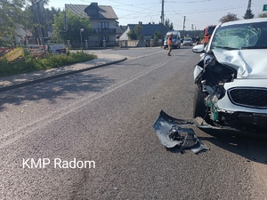 Miejsce zdarzenia drogowego w miejscowości Wojciechów. Na zdjęciu widoczny pojazd osobowy koloru białego z uszkodzonym przodem pojazdu. W tle radiowóz.