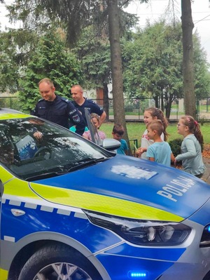 Policjanci stoją przy radiowozie, a dzieci oglądają policyjne auto.