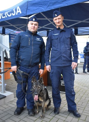 Na zdjęciu stoją dwaj policjanci w mundurach, Komendant i policyjny przewodnik z psem
