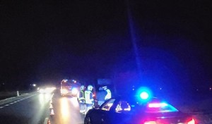 wieczór, nieoznakowany radiowóz na miejscu wypadku, w tle policjanci i strażacy