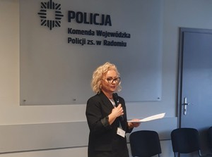 pracownica kadr trzyma mikrofon mówi o naborze do służby, w tle napis Komenda Wojewódzka Policji.
