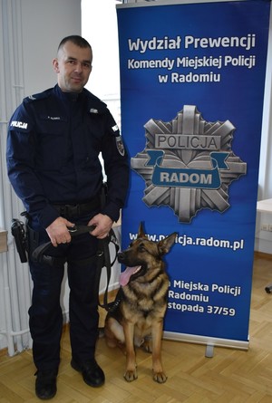 policyjny przewodnik z psem stoi na tle baneru z napisem Wydział prewencji